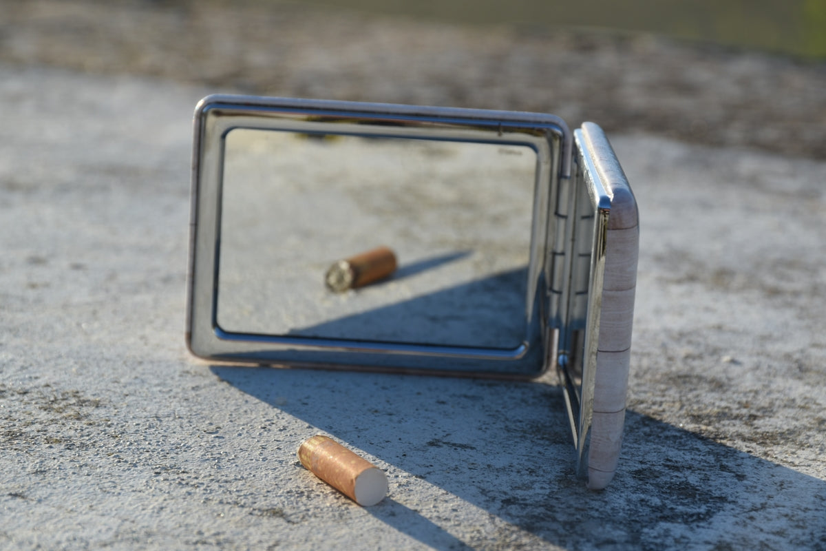 a broken mirror sitting on the ground next to a cigarette