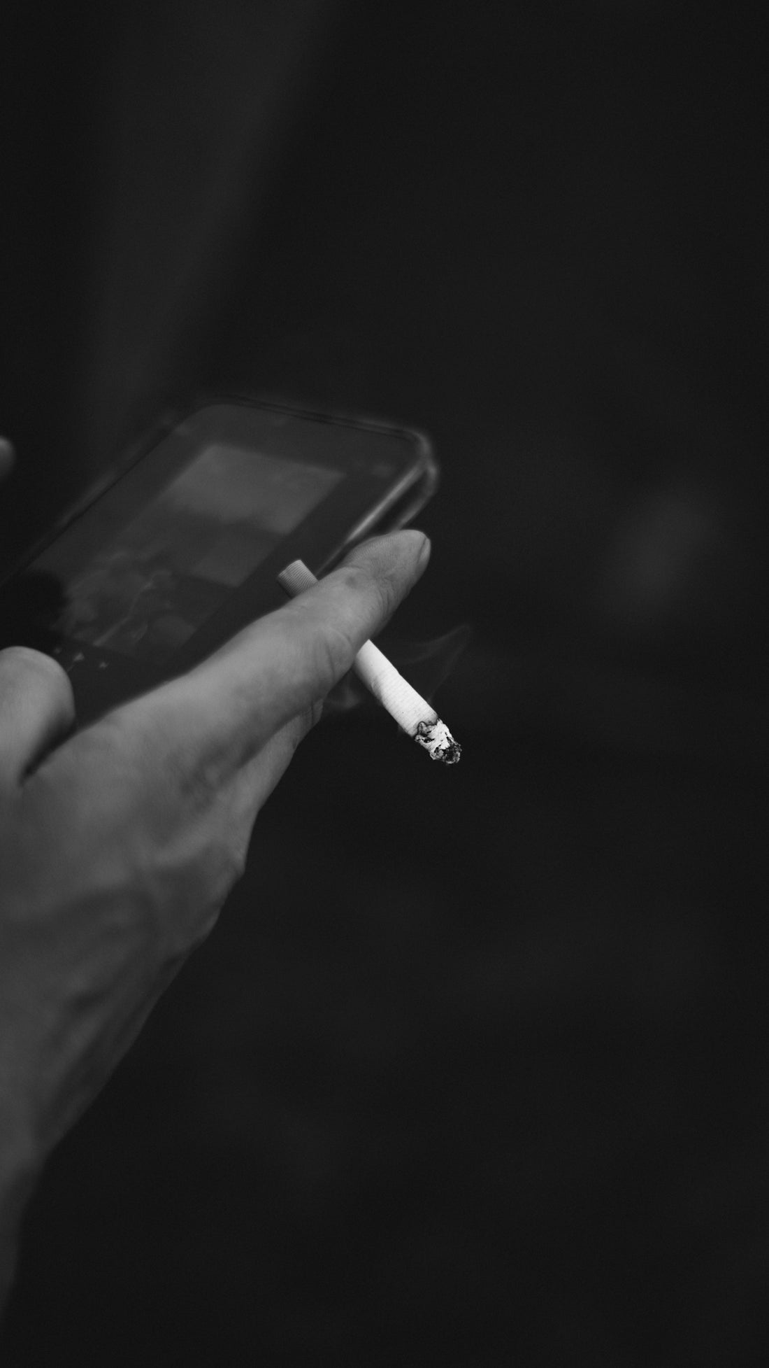 a person holding a smart phone with a cigarette in their hand